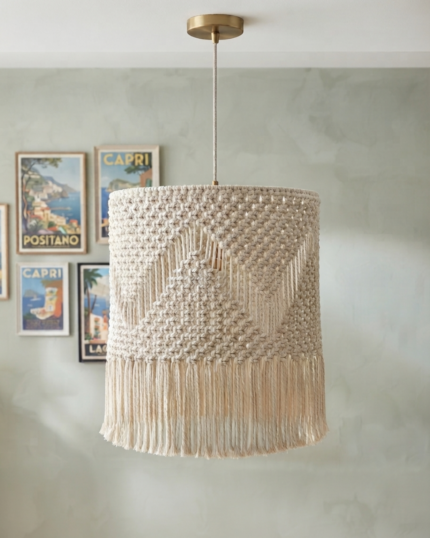 A frontal view of a handcrafted cream-colored macrame pendant light shade hanging from a white ceiling, showcasing a detailed geometric chevron knot pattern and a thick brushed straight cotton fringe at the bottom."