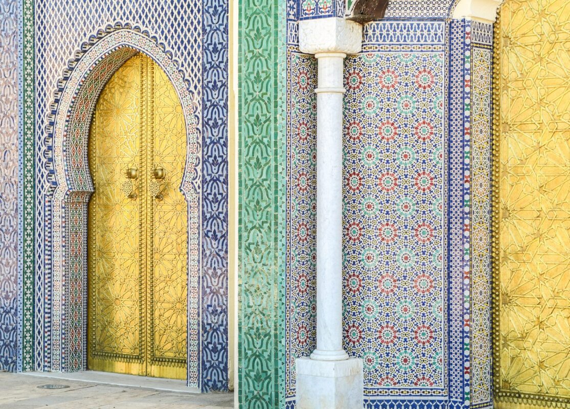 Golden brass palace door framed by blue and green Moroccan zellij mosaic tiles